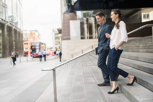 Side view of young businessman and woman chatting whilst walking down stairway, London, UK — Stock Photo