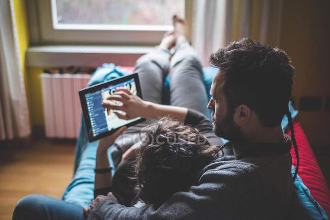 Пара, лежачи на дивані, використовуючи цифровий планшетний — стокове фото