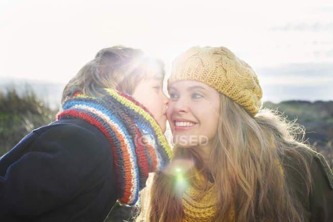 Взрослая женщина с сыном целуют ее щеку на побережье — стоковое фото