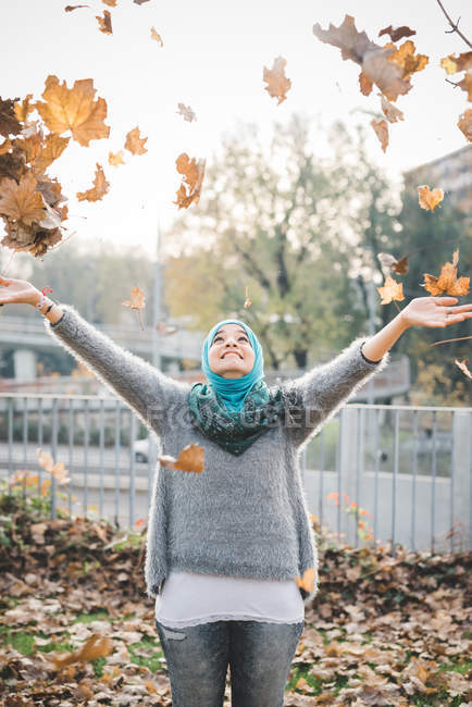 Молодая женщина в парке бросает осенние листья — стоковое фото