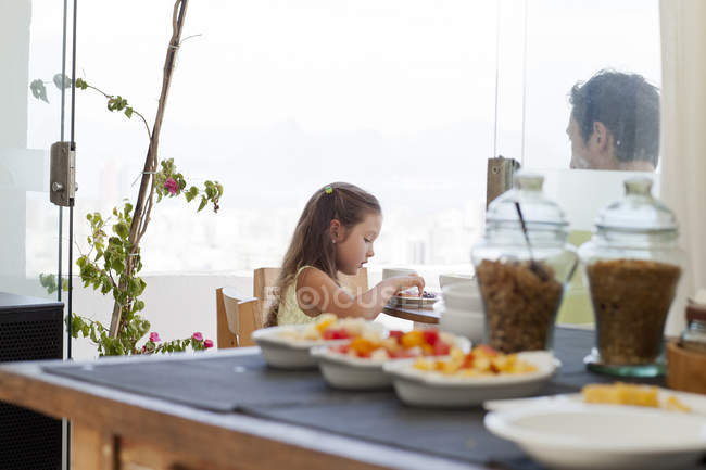 Father and daughter sitting at breakfast table on balcony, healthy food in foreground — Stock Photo