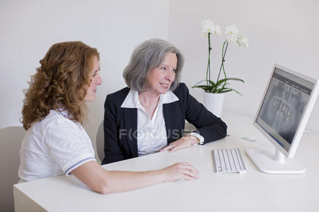 Mulher sênior e mulher madura na mesa discutindo imagem de raio-x na tela do computador sorrindo — Fotografia de Stock
