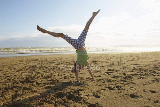 Девушка делает стойку на руках на пляже, Camber Sands, Кент, Великобритания — стоковое фото
