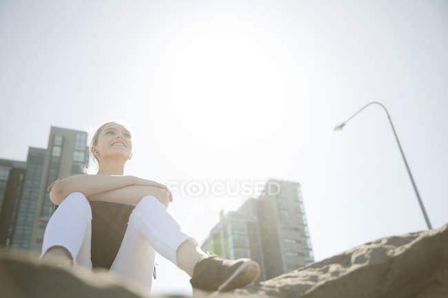 Низкий угол обзора высотных зданий и девочка-подросток, сидящая на скалах и улыбающаяся, Рейкьявик, Исландия — стоковое фото