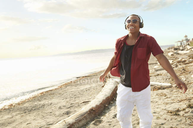 Jeune homme debout sur la plage portant écouteurs et lunettes de soleil — Photo de stock