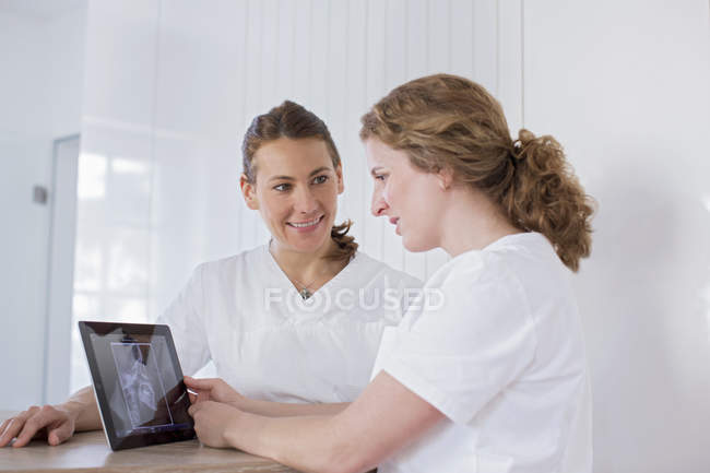 Стоматологи дивляться на цифровий планшет з рентгенівським зображенням на екрані, посміхаючись — стокове фото