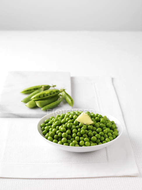 Raw pea pods on marble cutting board and bowl of boiled peas with butter — Stock Photo