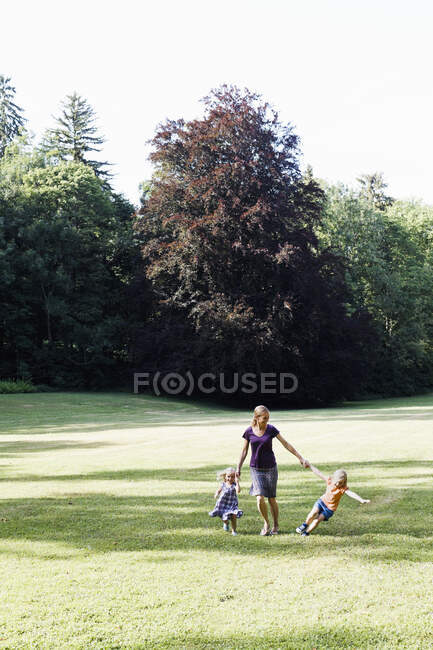 Взрослая женщина и две дочери держатся за руки и бегают в парке — стоковое фото