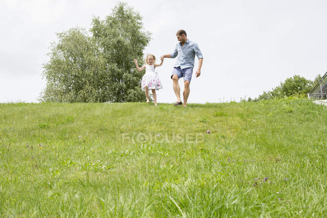 Отец и дочь бегут по склону с зеленым лугом — стоковое фото