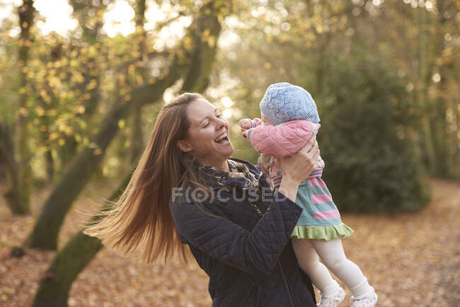 Mid adult woman swinging baby daughter in autumn park — Stock Photo