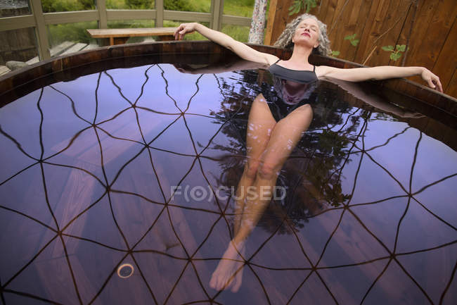 Mulher madura deitada de volta na banheira de hidromassagem no retiro ecológico — Fotografia de Stock