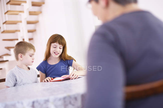 Бабуся дивляться онуків прочитати книгу в кухонному столі — стокове фото
