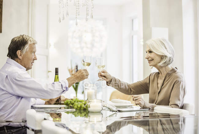 Couple âgé assis ensemble à table, tenant des verres à vin, portant un toast — Photo de stock