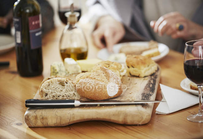 Gros plan de pain fraîchement cuit sur planche à découper, femme mangeant sur fond — Photo de stock