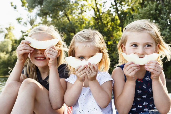 Retrato de três jovens irmãs segurando melão sorridente na frente do rosto no parque — Fotografia de Stock