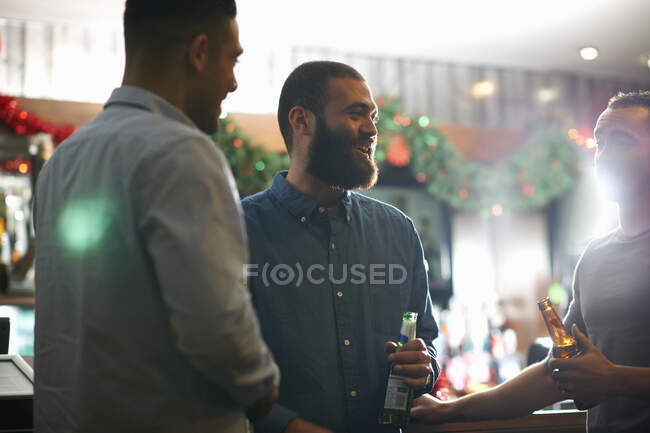 Young men in public house holding beer bottles leaning against counter smiling — Stock Photo
