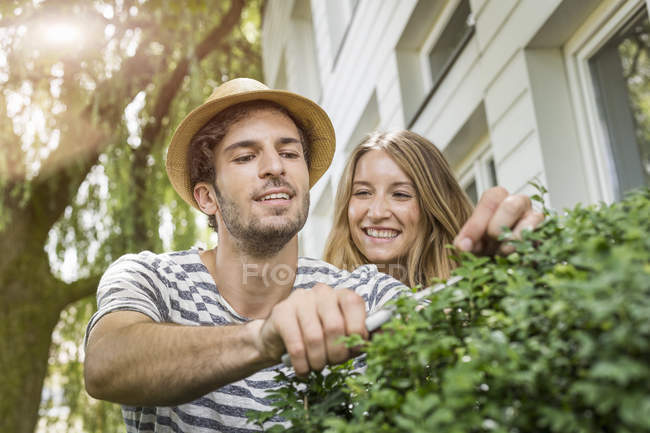 Молодая пара обрезает кусты у дома — стоковое фото