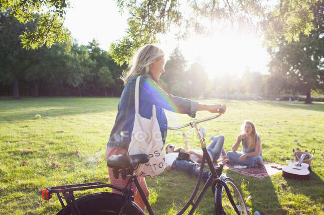 Young woman arriving on bicycle to sunset park party — Stock Photo