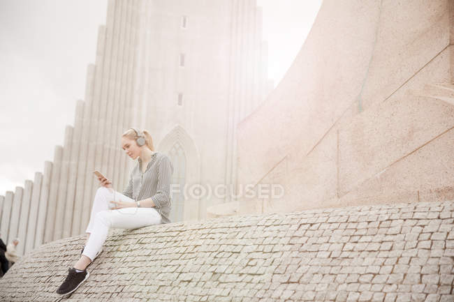 Jeune femme blonde assise près du clocher de l'église et écoutant de la musique, Reykjavik, Islande — Photo de stock