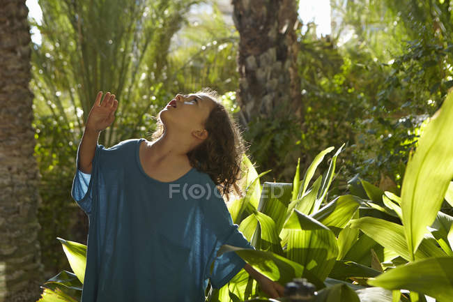 Young girl looking up at green trees foliage — Stock Photo