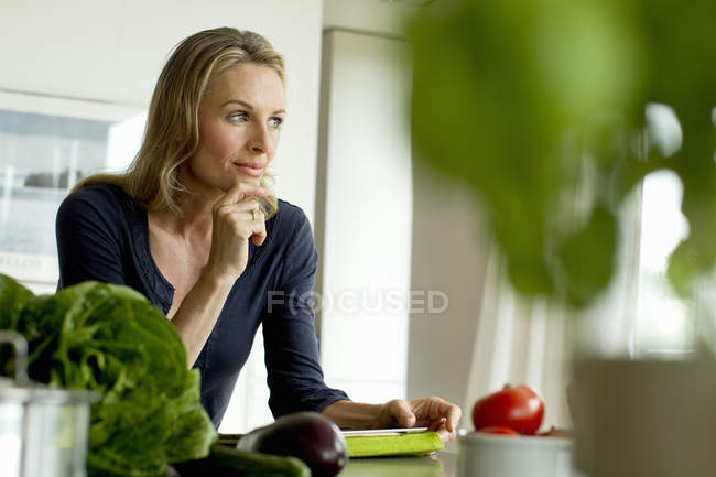 Зріла жінка з цифровим планшетом сидить за столом — стокове фото