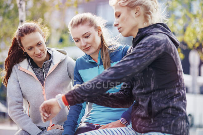 Three female runners coordinating times on smartwatch in city — Stock Photo