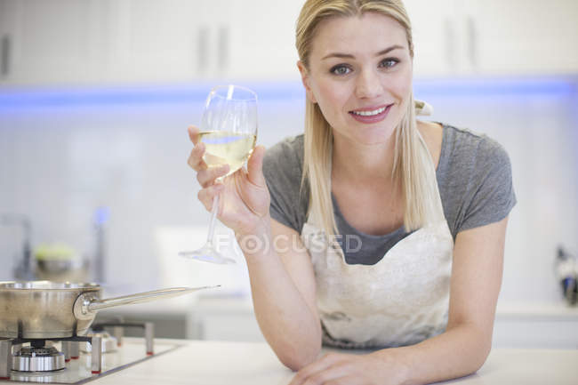 Retrato de jovem mulher bebendo copo de vinho branco na cozinha — Fotografia de Stock