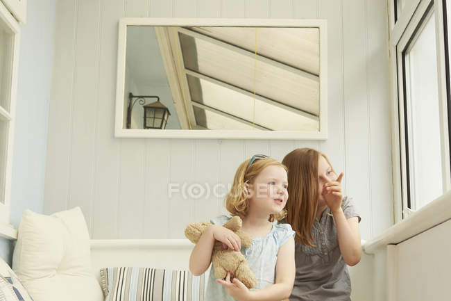 Two sisters pointing and looking out of holiday apartment window — Stock Photo