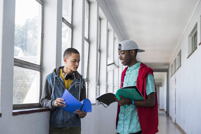 Students standing in hallway and looking at textbooks — Stock Photo