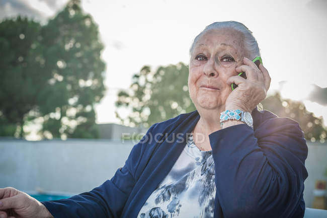 Старша жінка використовує смартфон на задньому дворі — стокове фото