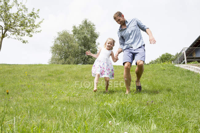 Pai e filha correndo descida na grama verde — Fotografia de Stock