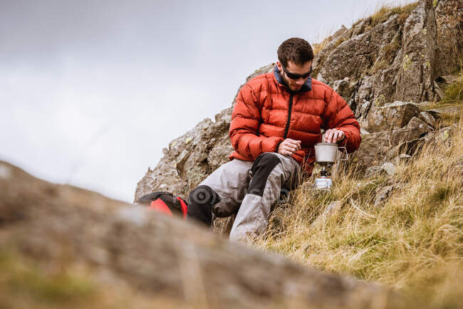 Young male hiker igniting camping stove, The Lake District, Cumbria, UK — Stock Photo