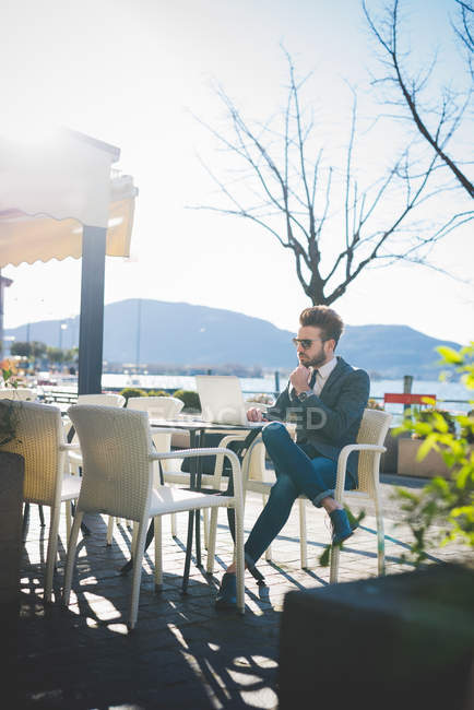 Empresario que usa laptop en lakeside café, Rovato, Brescia, Italia - foto de stock