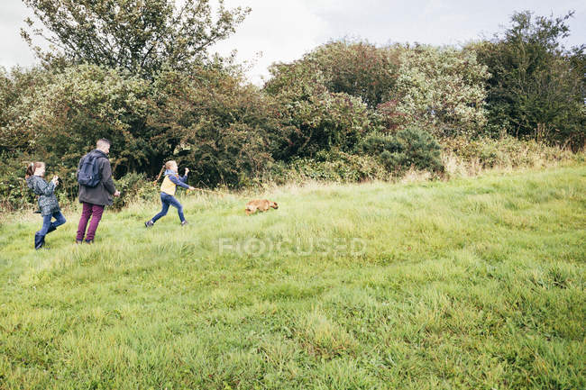 Padre y dos niñas paseando perro en el campo - foto de stock
