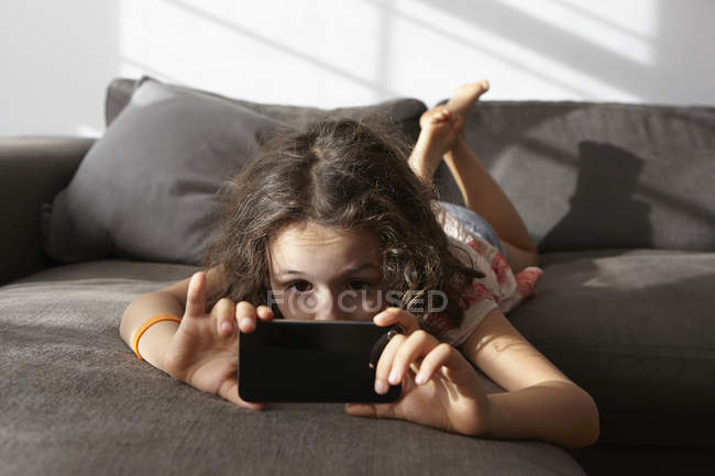 Дівчина лежить на дивані у вітальні, дивлячись на смартфон — стокове фото