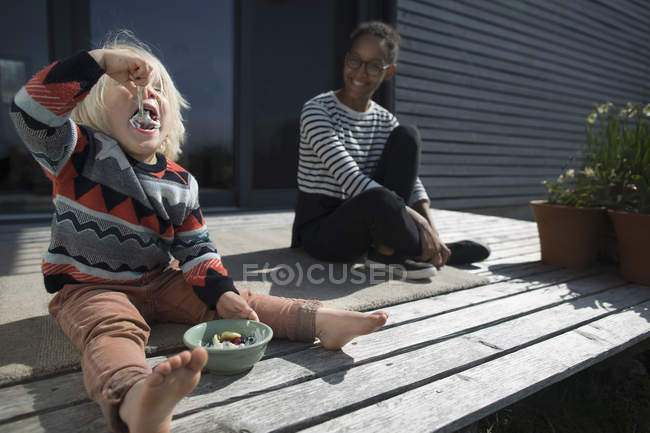 Boy sitting on wooden decking eating from bowl — Stock Photo