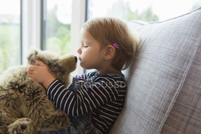 Kleinkind sitzt auf Sofa und küsst Teddybär — Stockfoto
