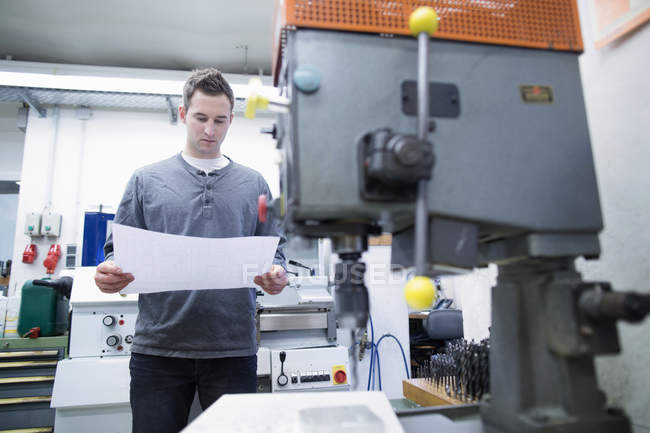 Young male technician looking at blueprint in workshop — Stock Photo