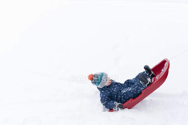 Junge spielt auf seinem Schlitten im Schnee — Stockfoto