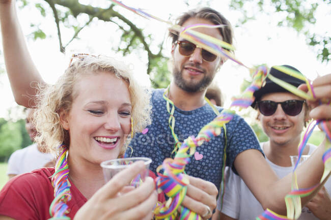 Amigos adultos envolvendo uns aos outros em streamers na festa do pôr do sol no parque — Fotografia de Stock