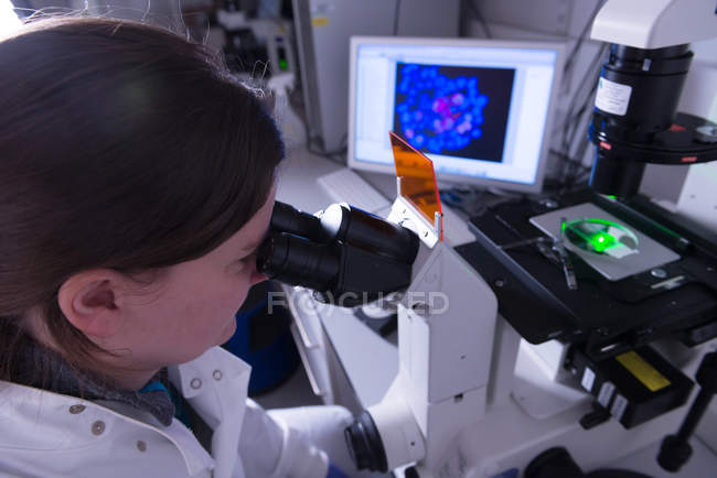 Лаборатория исследования рака, женщина-ученый изучает электронный микроскоп — стоковое фото