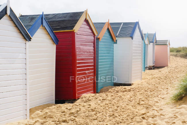 Row of multi colored beach huts on sand — Stock Photo