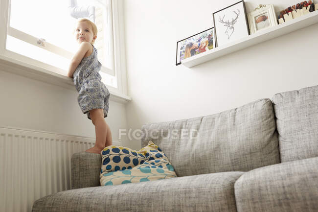 Vista a basso angolo del bambino femmina in piedi sul divano dalla finestra — Foto stock