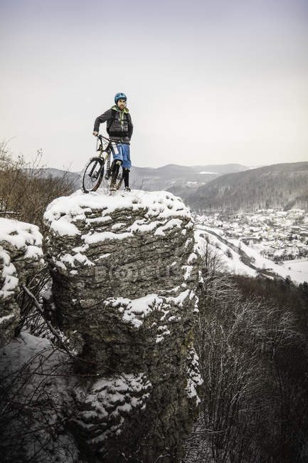 Joven ciclista de montaña en la parte superior de la formación de rocas cubiertas de nieve - foto de stock