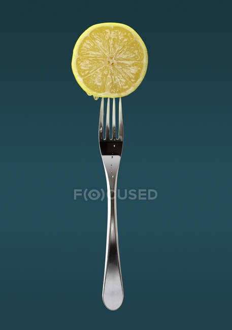 Frische Zitronenscheibe auf Gabel auf blauem Hintergrund — Stockfoto