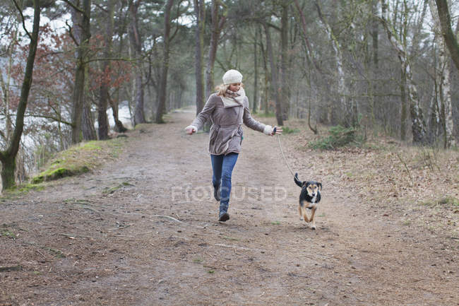 Mitte erwachsene Frau läuft mit Hund im Wald — Stockfoto