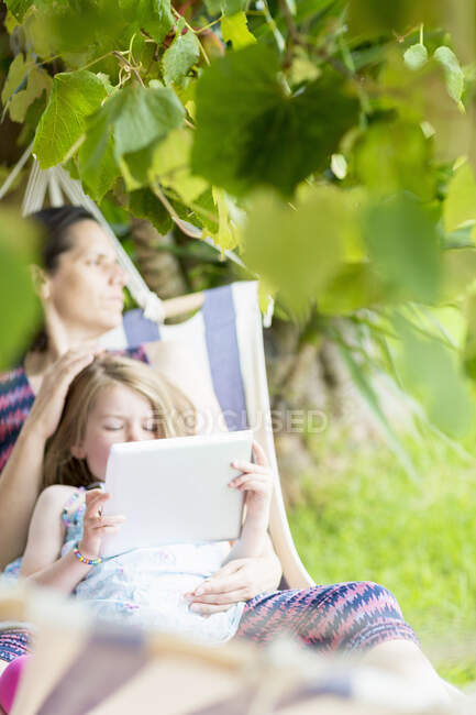 Дочь сидит на коленях у матери с помощью цифрового планшета — стоковое фото