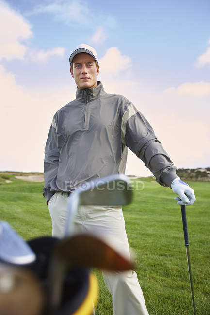Golfer holding gold club, hand in pocket, looking at camera — Stock Photo
