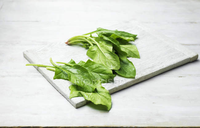 Whole leaves of spinach on wooden chopping board — Stock Photo