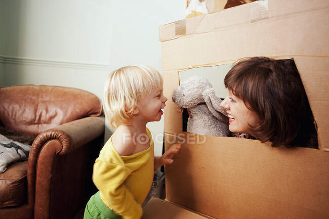Mother and son playing with cardboard box window in living room — Stock Photo